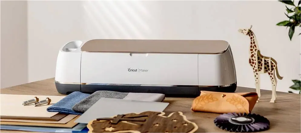 Machine de découpe Cricut Maker entourée de matériaux découpés : bois, feutrine, cuir et girafe en bois