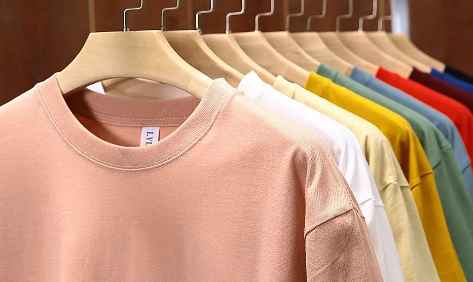 T-shirts vierges de différentes couleurs sur cintres en bois, prêts à personnaliser