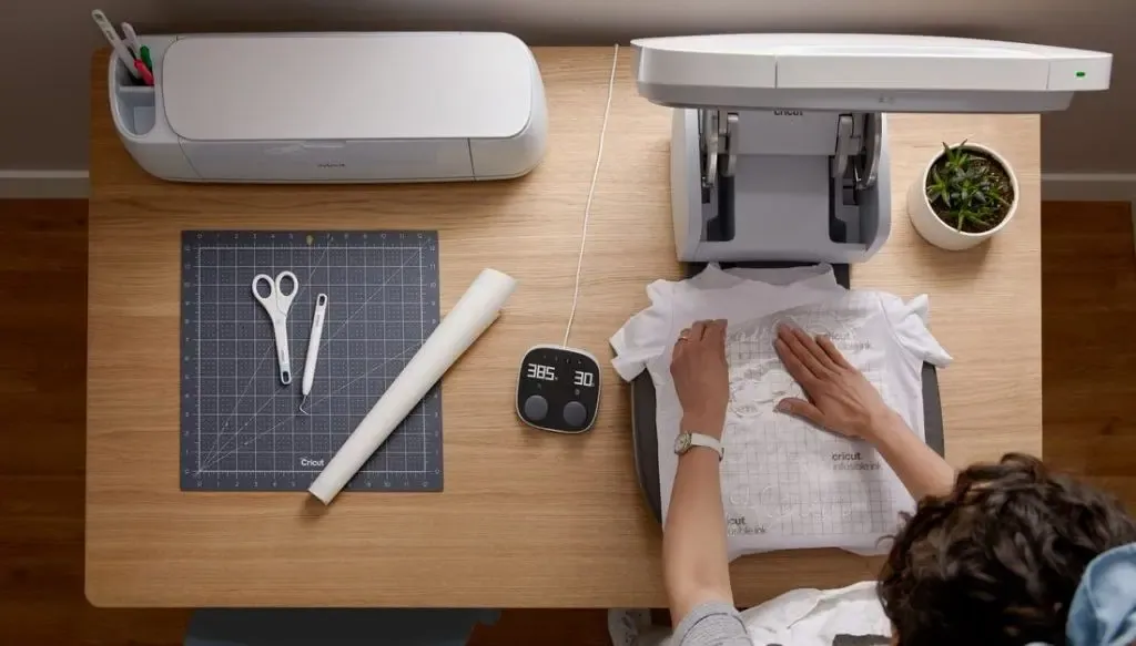 Atelier vu de dessus : t-shirt posé sur la Cricut AutoPress, machine Cricut, tapis et boîtier de commande