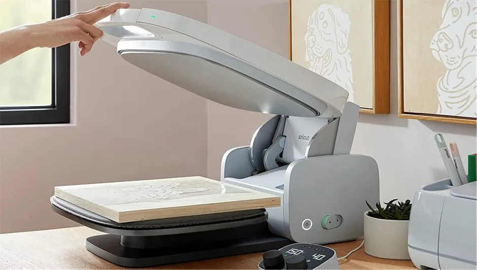 Main sur le plateau relevé de la presse à chaud Cricut AutoPress, planche en bois décorée prête à presser