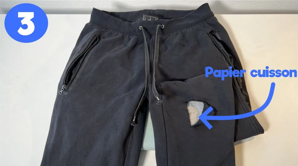 Étape 3 : feuille de papier cuisson glissée dans le pantalon noir, sous le trou à réparer