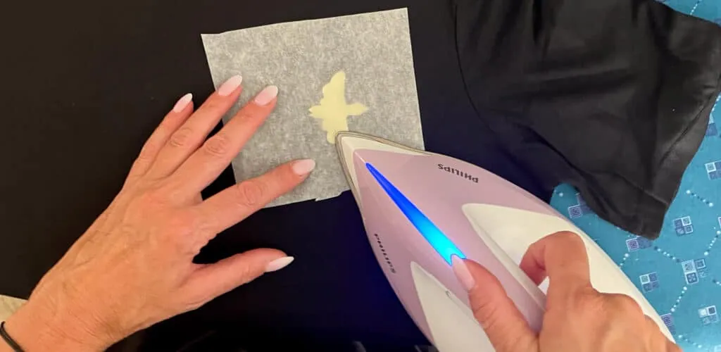 Pressage au fer d'un motif en flex jaune sur un t-shirt noir, protégé par une feuille de papier cuisson