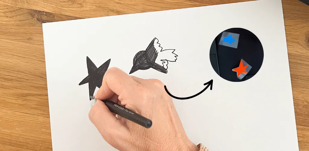 Main dessinant une étoile et un oiseau au feutre, flèche vers ces motifs en flex posés sur un cartable noir