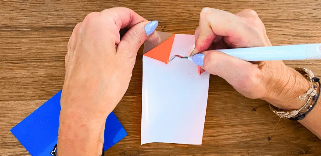 Échenillage au crochet d'un motif en flex orange sur son support transparent, chute de flex bleu à côté