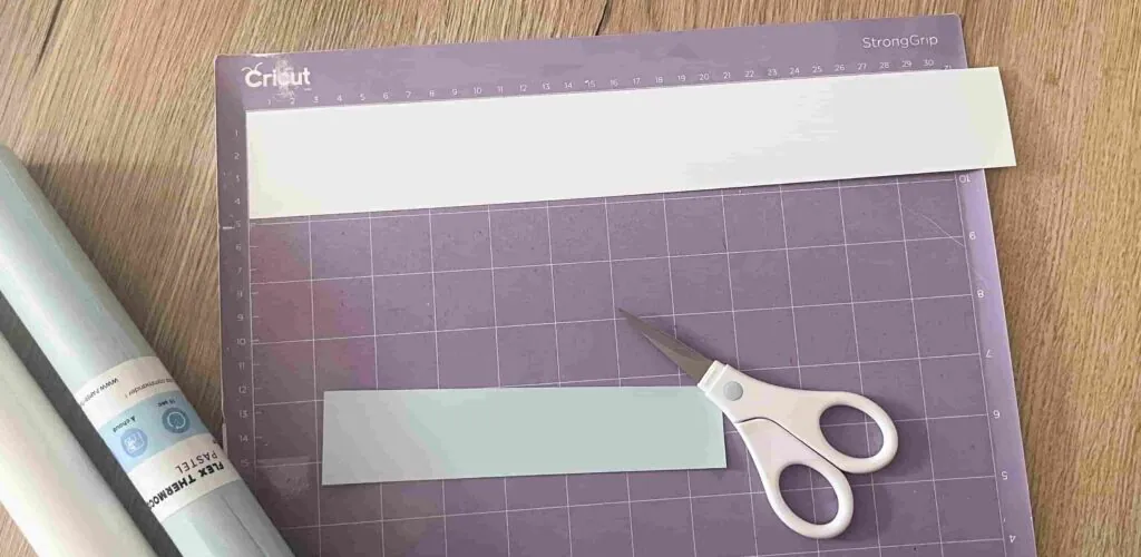 Bandes de flex thermocollant pastel collées sur un tapis de découpe Cricut StrongGrip violet, ciseaux à côté
