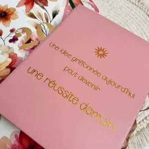 Carnet rose orné en doré de « Une idée griffonnée aujourd'hui peut devenir une réussite demain »