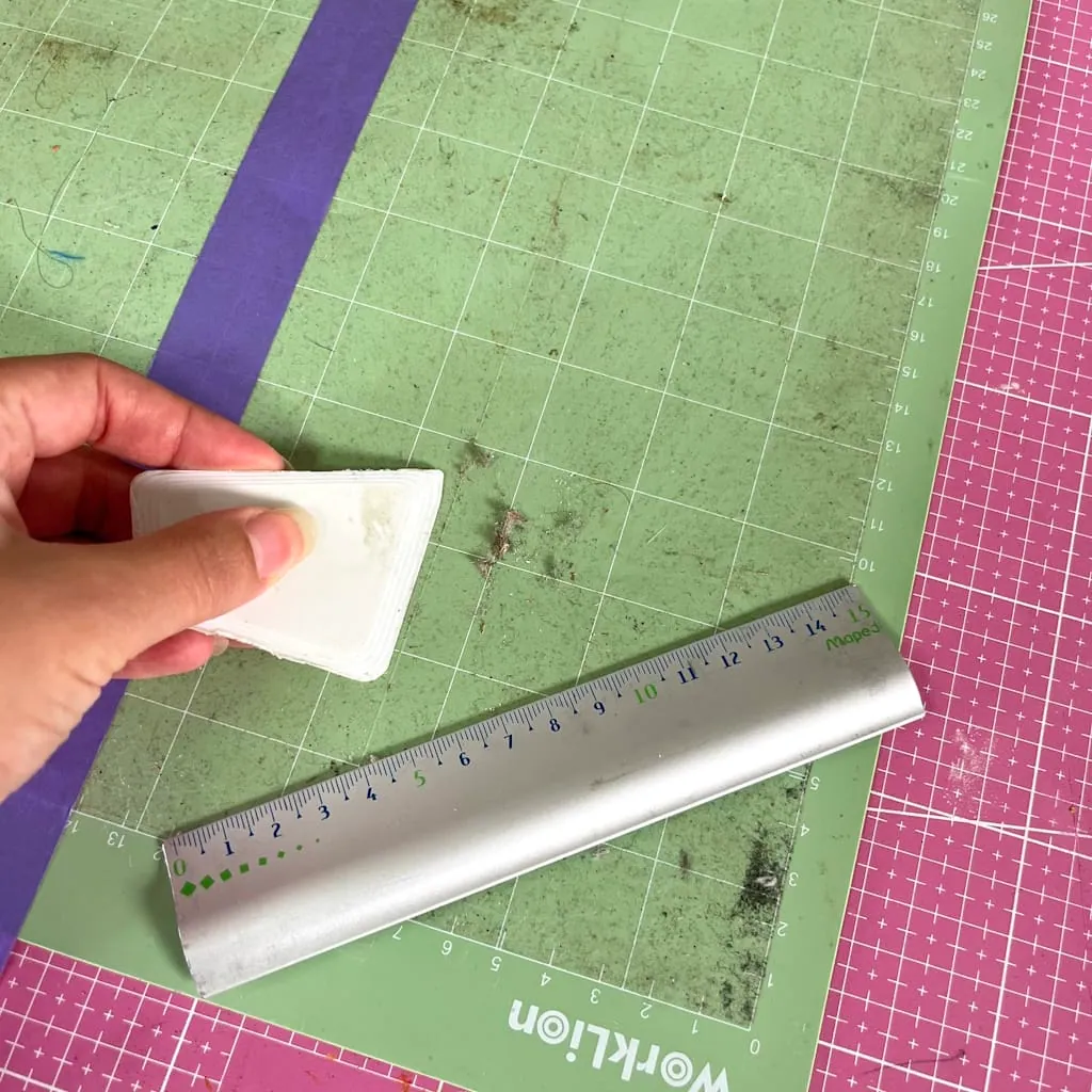 Grattoir en plastique retirant les résidus d'un tapis de découpe vert, règle métallique posée dessus