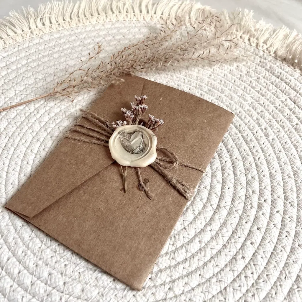 Faire-part de mariage terminé : pochette kraft fermée par une ficelle, un cachet de cire et des fleurs séchées