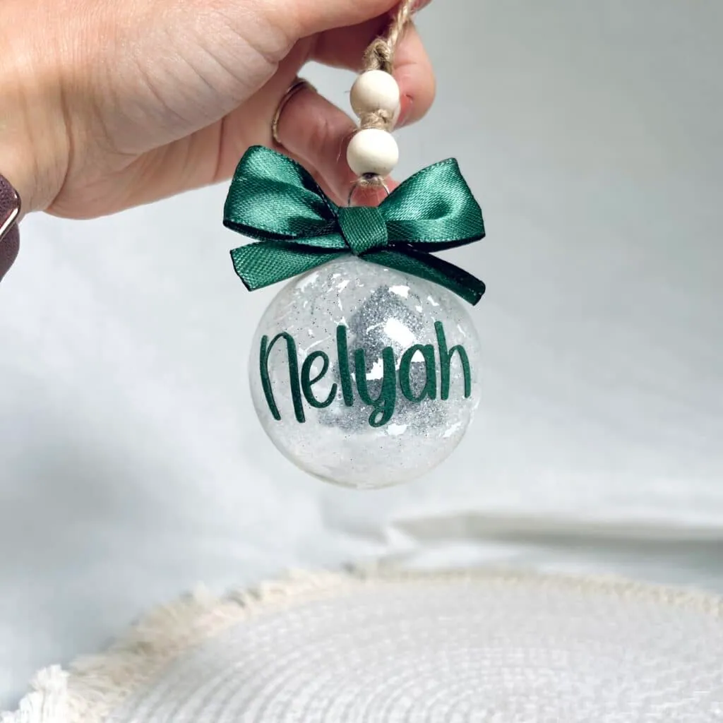 Boule de Noël transparente pailletée au prénom Nelyah en vinyle vert, avec nœud vert et perles en bois