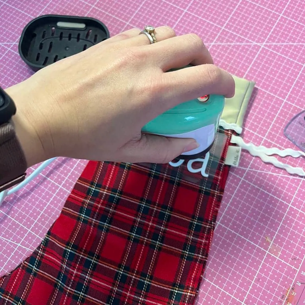 EasyPress Mini pressant le prénom en flex blanc sur une chaussette de Noël en tartan rouge